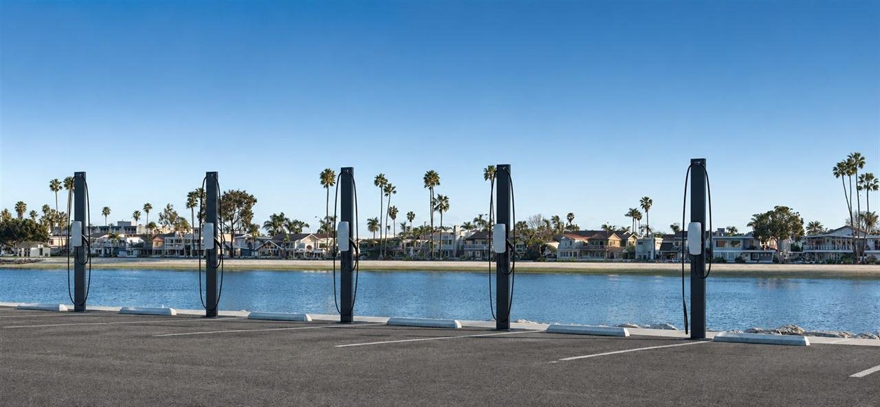 A row of five pedestal-mounted Tesla Wall Connectors in a waterfront car park