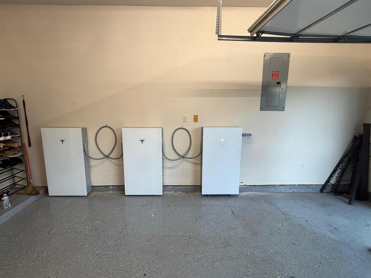 Three Tesla Powerwall 3 units installed side by side on a garage wall beside the main electrical panel
